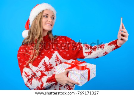 Smiling cheerful happy attractive girl is making a self portrait with a present box, isolated on bright blue background