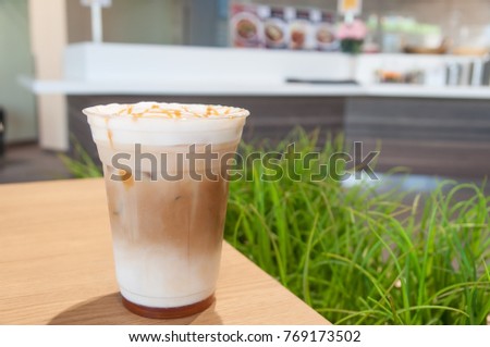 Gold caramel topping on white cream in coffee cup with green grass background.
