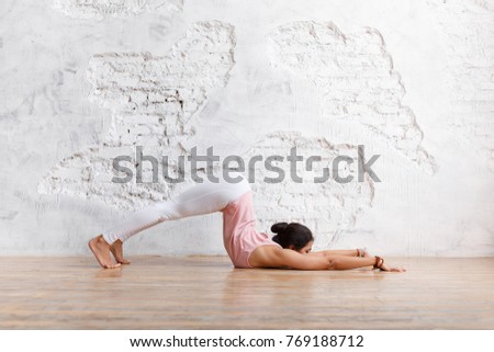 Side view - sports unidentified young woman doing complex yoga exercise stretching her legs and arms in the gym on white wall background. Copy space Royalty-Free Stock Photo #769188712