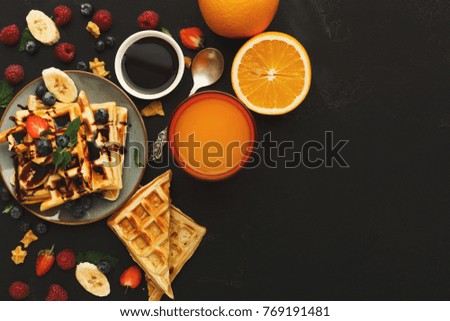 Belgian waffles with berries and fruits on black background. Top view on checkered biscuits with chocolate topping, orange and juice copy space. Sweet food and tasty breakfast concept
