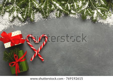 Christmas gift boxes in colorful wrapping paper with traditional xmas lollipops heart on gray background with fir frame, top view, copy space