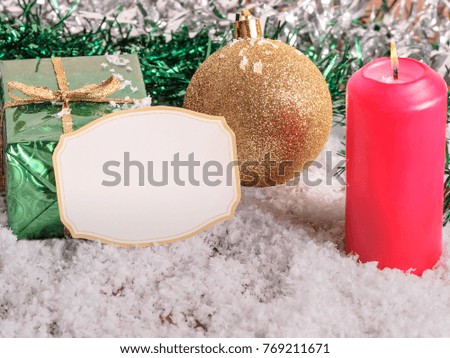 Background with Christmas balls, a red candle and a small green box on the snow