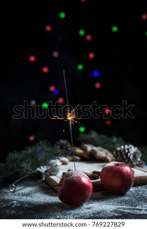 apples and gingerbread for the new year on a silver tray, New Year's lights, fireworks, fur-tree, cones, cinnamon on a wooden cutting board, on a dark background