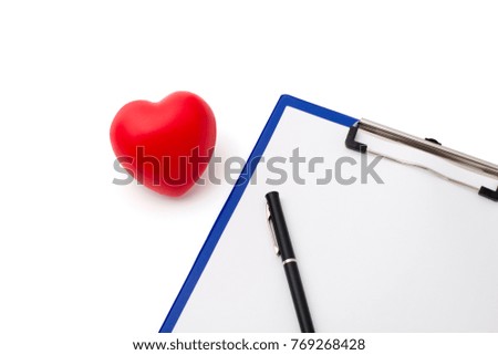 Red rubber heart beside a clipboard and pen on white background; concept of health, cardio examination