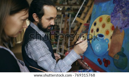 Skilled artist man teaching young girl to draw paintings and explaining the basics of light in art studio