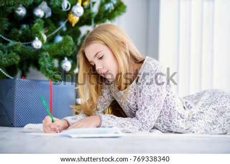 Cute girl near the Christmas tree writing a letter to Santa Claus. Christmas concept. Belief in miracles.