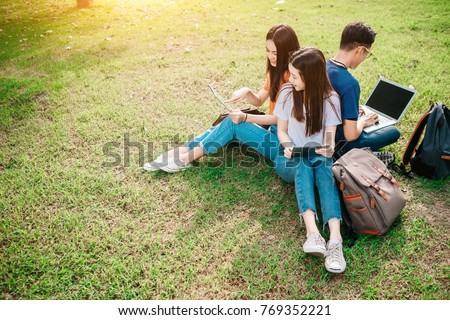 A group of young or teen Asian student in university smiling and reading the book and look at the tablet or laptop computer in summer holiday. Royalty-Free Stock Photo #769352221