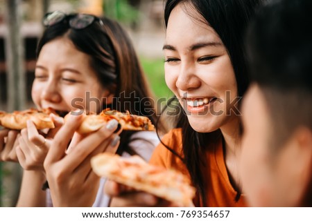 Asian students eating eating the pizza together in breaking time early next study class having fun and enjoy party, Italian food slice with cheese delicious at university outdoor. Royalty-Free Stock Photo #769354657