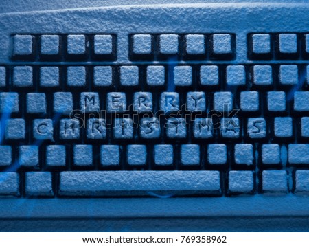 computer keyboard with text merry christmas on buttons covered with snow illuminated by blue neon light