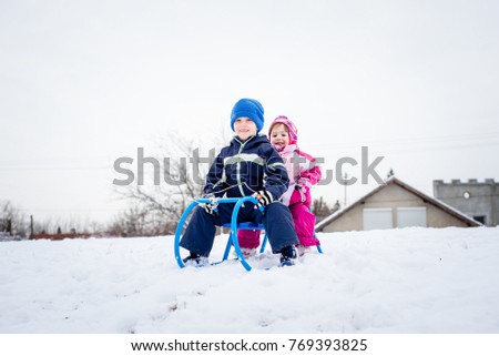 Two smiling children sitting on sled.
