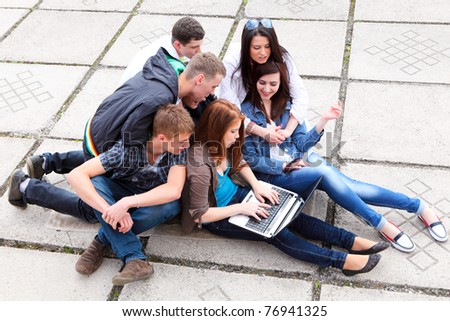 Group of male and female students sitting with a laptop on street Royalty-Free Stock Photo #76941325
