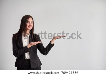 Smiling young businesswoman, showing something, some product or blank copyspace area for advertise slogan or text message, on a gray wall in the office