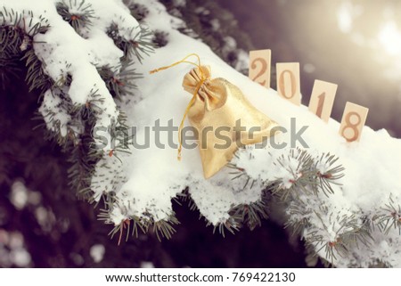 shiny bag on snow-covered fir branch against the background of blurry new year figures / golden gift for a holiday