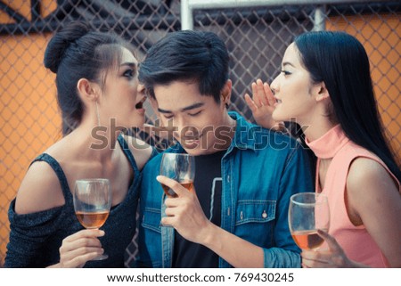 Women whispering in man's ear and  holding glasses of alcohol drinks.