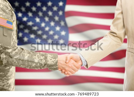 American soldier in uniform and civil man in suit shaking hands with adequate national flag on background - United States of America