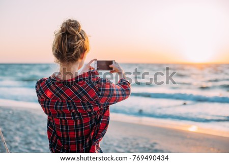 young woman taking photos with her smartphone on beach during sunset or sunrise