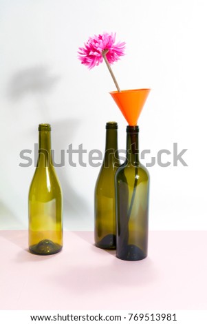 3 brown green glass bottles isolated on a bicolor background. a funnel with pink flower inside. Minimal wacky color still life photography
