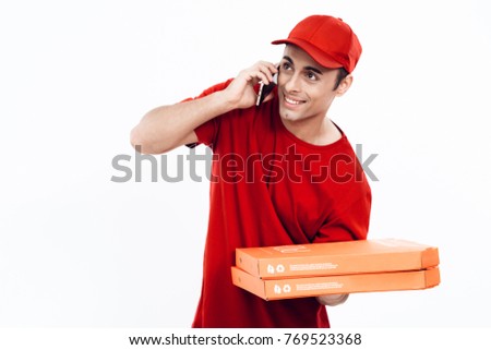 A man of Arab appearance works in the delivery of pizza. A man in a red uniform is holding a box of pizza in his hands and posing against a white background.