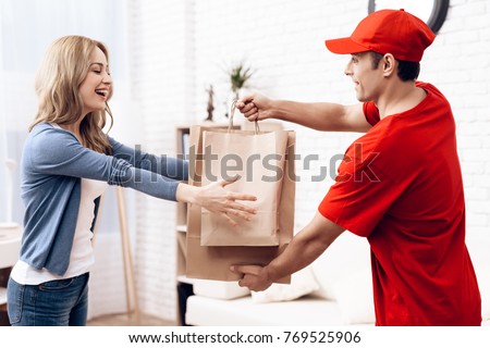 A man of Arab nationality works in delivery. The girl received the parcel delivery to the house. A man in red clothes brought a package to a young woman. Royalty-Free Stock Photo #769525906