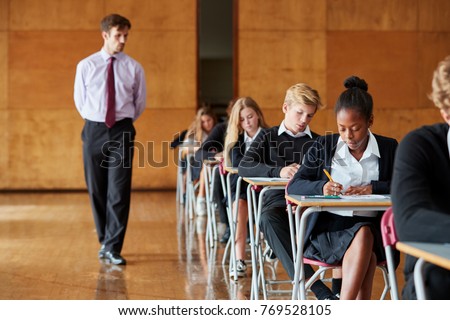 Teenage Students Sitting Examination With Teacher Invigilating Royalty-Free Stock Photo #769528105
