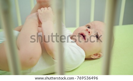 Baby's lying on a green linen in a crib at home, and crying. Soft focus close-up.