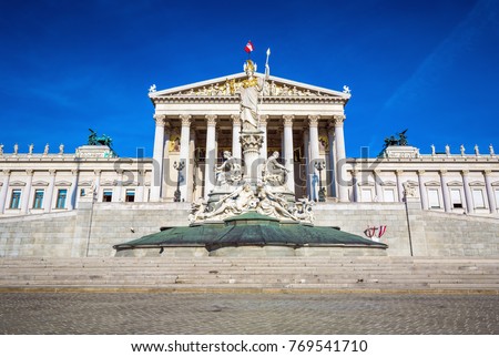  Austrian parliament building in Greek style with statues of philosophers and white columns with famous Pallas Athena fountain in Vienna.