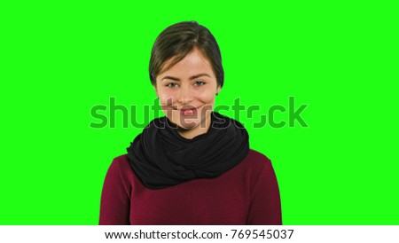 A young modest lady smiling and closing her eyes against a green background. Medium shot