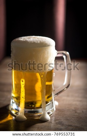Glass with beer. Light beer. The foam flows down a glass. A glass of beer is on the table.
