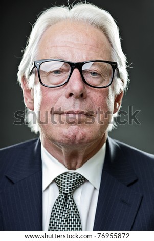 Studio portrait of serious senior man in suit wearing glasses.