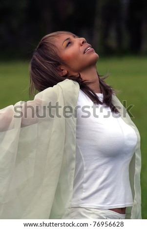 A beautiful mature black woman soaks up some atmosphere and celebrates with a swatch of sheer fabric outdoors.