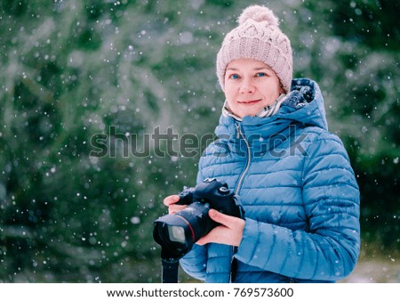 Portrait of beautiful smiling young woman with camera on winter snow day
