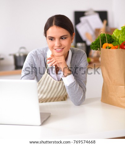 Beautiful young woman cooking looking at laptop screen with receipt in the kitchen