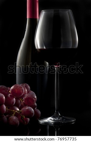 Glass of red wine with bottle and grapes on black background