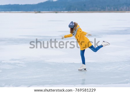 Young beautiful girl in yellow jacket is skating at winter on a frozen lake. Girl performs figure skating tricks.