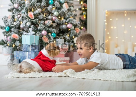 little boy and dog in Santa costume lying by the fireplace by the decorated Christmas tree with gifts