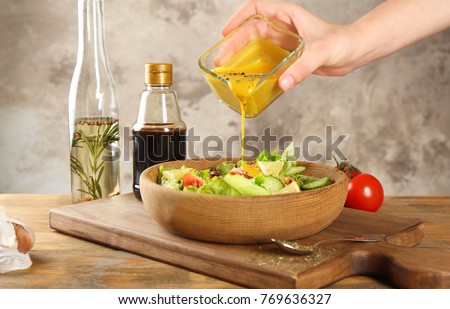 Woman pouring honey mustard dressing into bowl with fresh salad on table Royalty-Free Stock Photo #769636327