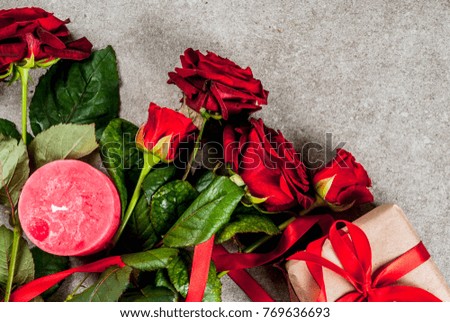 Holiday  background, Valentine's day. Bouquet of red roses, tie with a red ribbon, with wrapped gift box and red candle. On a gray stone table, copy space top view
