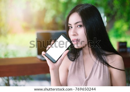 Mockup image of a beautiful woman holding and showing white mobile phone with blank black screen and smiley face in vintage cafe