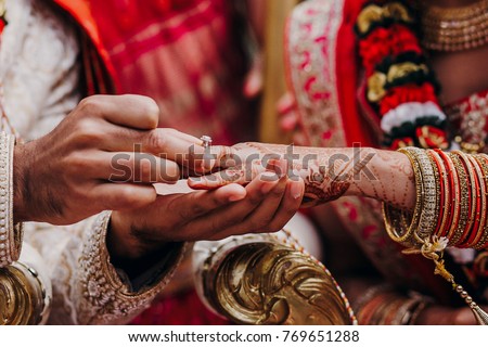 Tender hands of an Indian bride covered with henna tattoo hold groom's hand while he gives her a wedding ring Royalty-Free Stock Photo #769651288