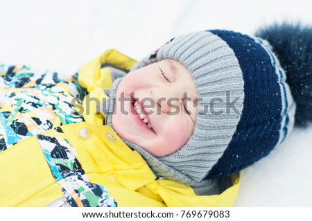 Little boy playing in the snow, portrait, lying on his back, laughing