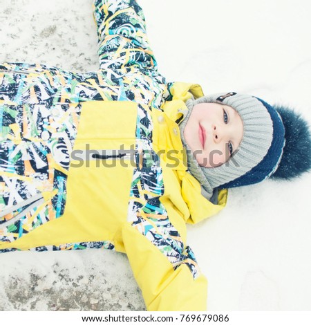 Little boy playing in the snow, portrait, lying on his back, laughing