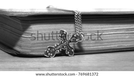 Black and white picture of a book and a metal cross on a wooden surface
