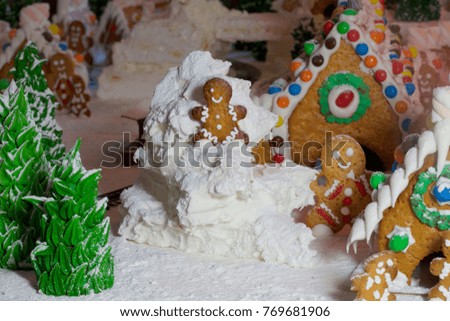 On a white wooden level are cottages made of Christmas gingerbread decorated with multicolored glaze and sweets. Color photo