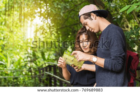 Young couple tourists looking at map while travelling to explore forest on clear day