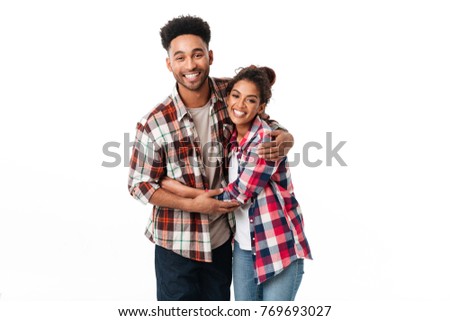Portrait of a happy young african couple hugging while standing together and looking at camera isolated over white background