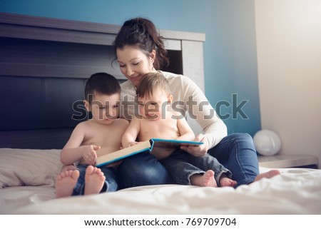 A mother reading a book with her two child boy in the bedroom