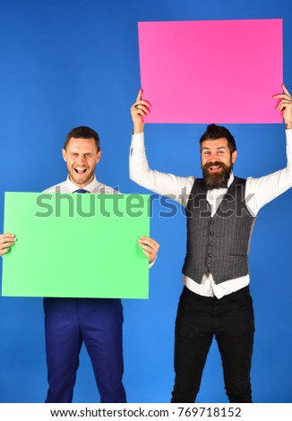 Happy smiling young businessmen showing blank green and pink signboards on blue background. Advertising concept