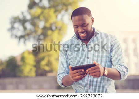 Modern gadget. Handsome pleasant nice man holding his smartphone and playing on it while being outside Royalty-Free Stock Photo #769729072