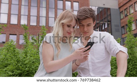 A young blonde couple using a smapthone outdoors. Soft focus. Medium shoot