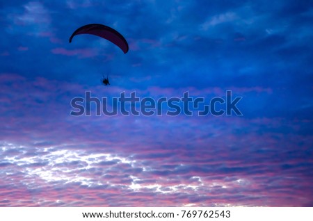 Motorized paraglider flying up high on the sky by the sunset